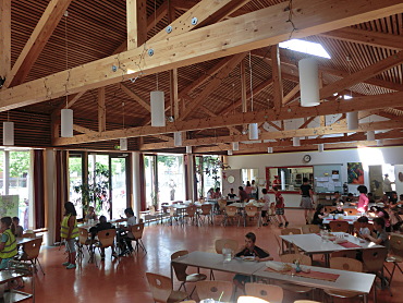 Hier sieht man unsere Mensa mit fröhlichen Kindern, die essen.